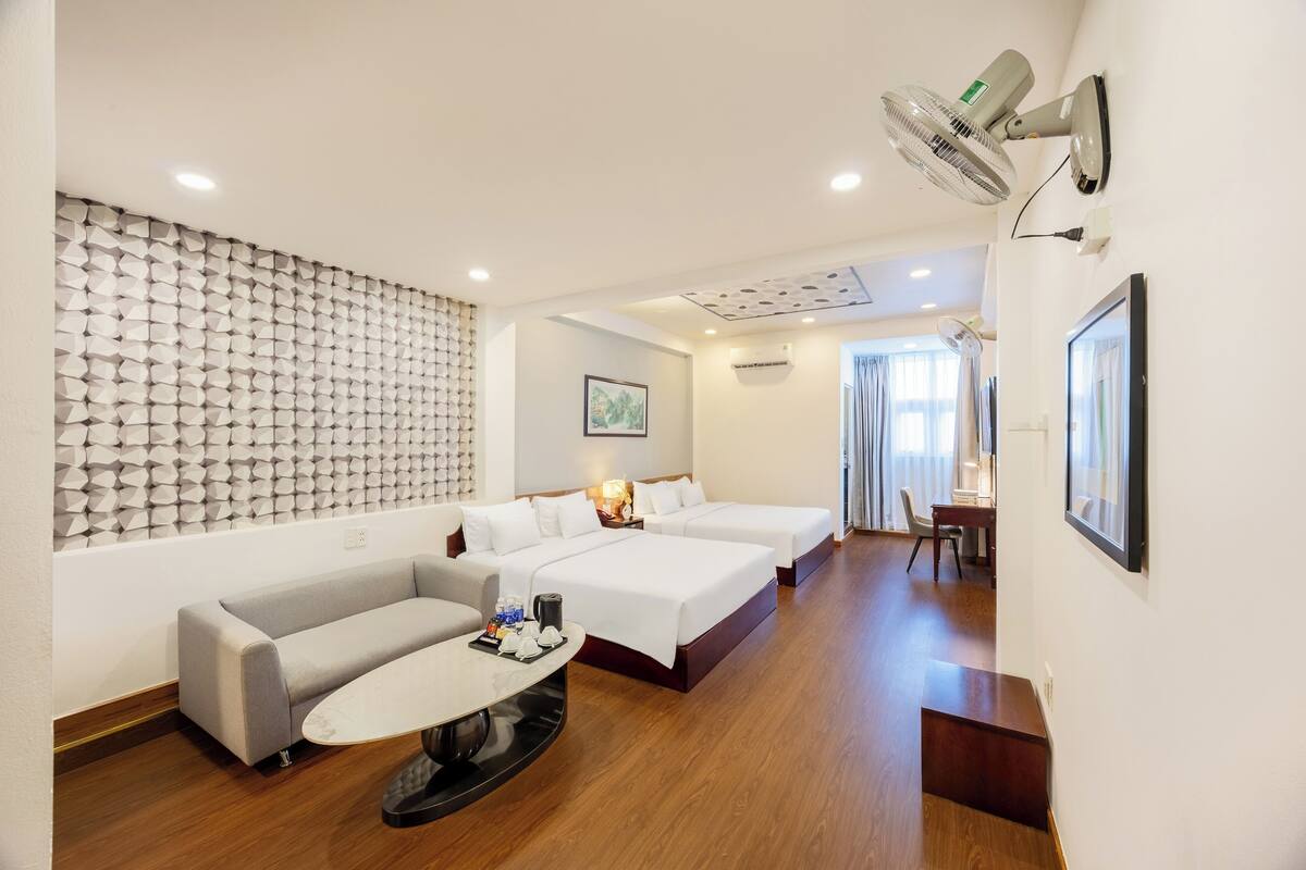 Une chambre d’hôtel avec un canapé, deux lits, une table à manger et un ventilateur fixé au mur.