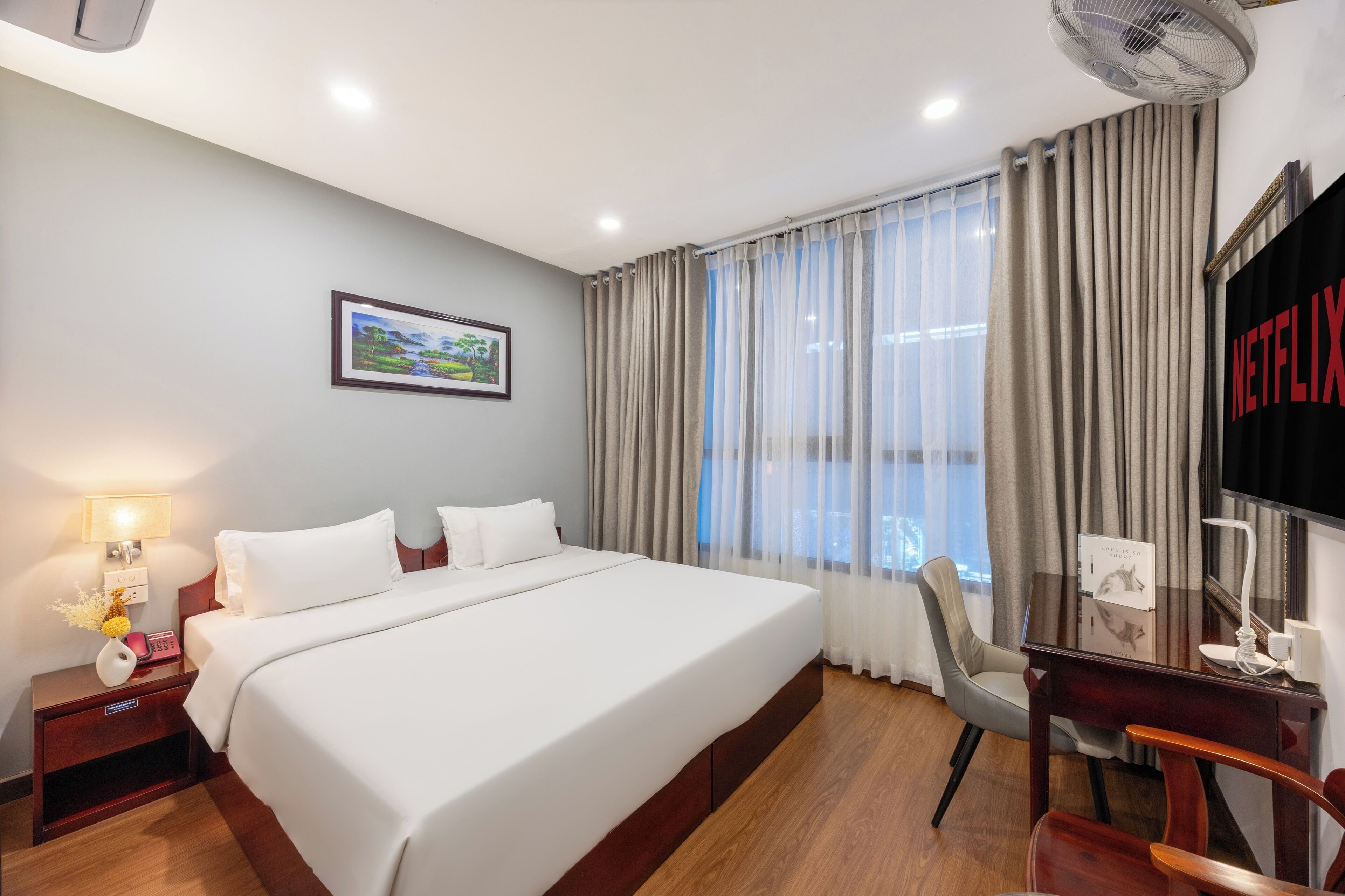 A hotel room with a large bed, a desk, a chair, a TV, and a picture on the wall.