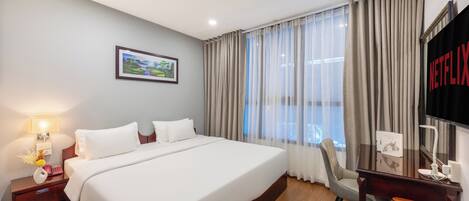 A hotel room with a large bed, a desk, a chair, a TV, and a picture on the wall.