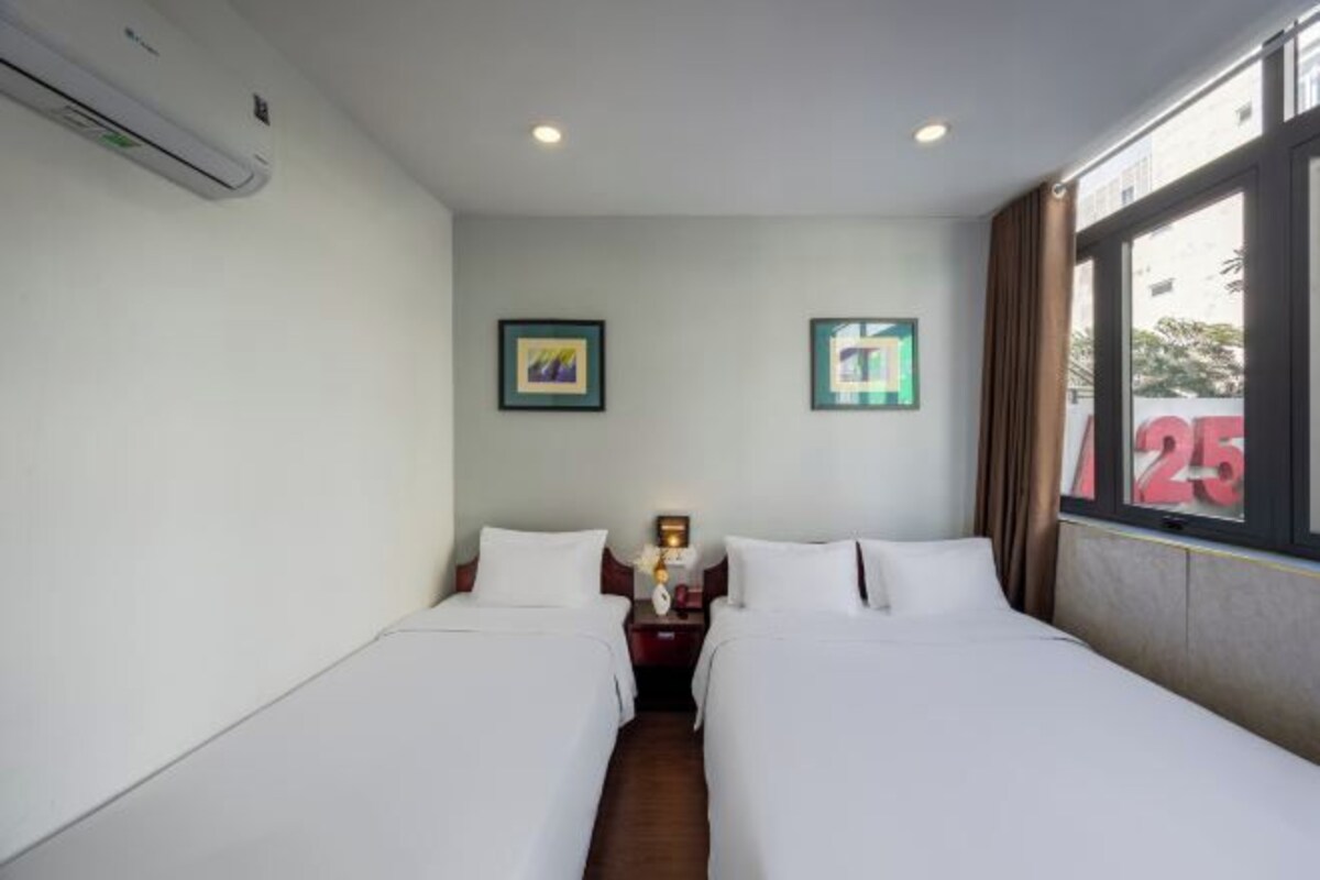 A hotel room with two beds, a nightstand, a wall-mounted air conditioner, and framed pictures on the wall.