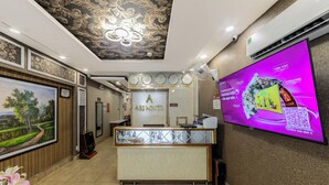 Un espace d’accueil d’hôtel comprenant un comptoir de réception, un grand écran de télévision affichant les services proposés par l’hôtel et un plafond orné de motifs floraux.