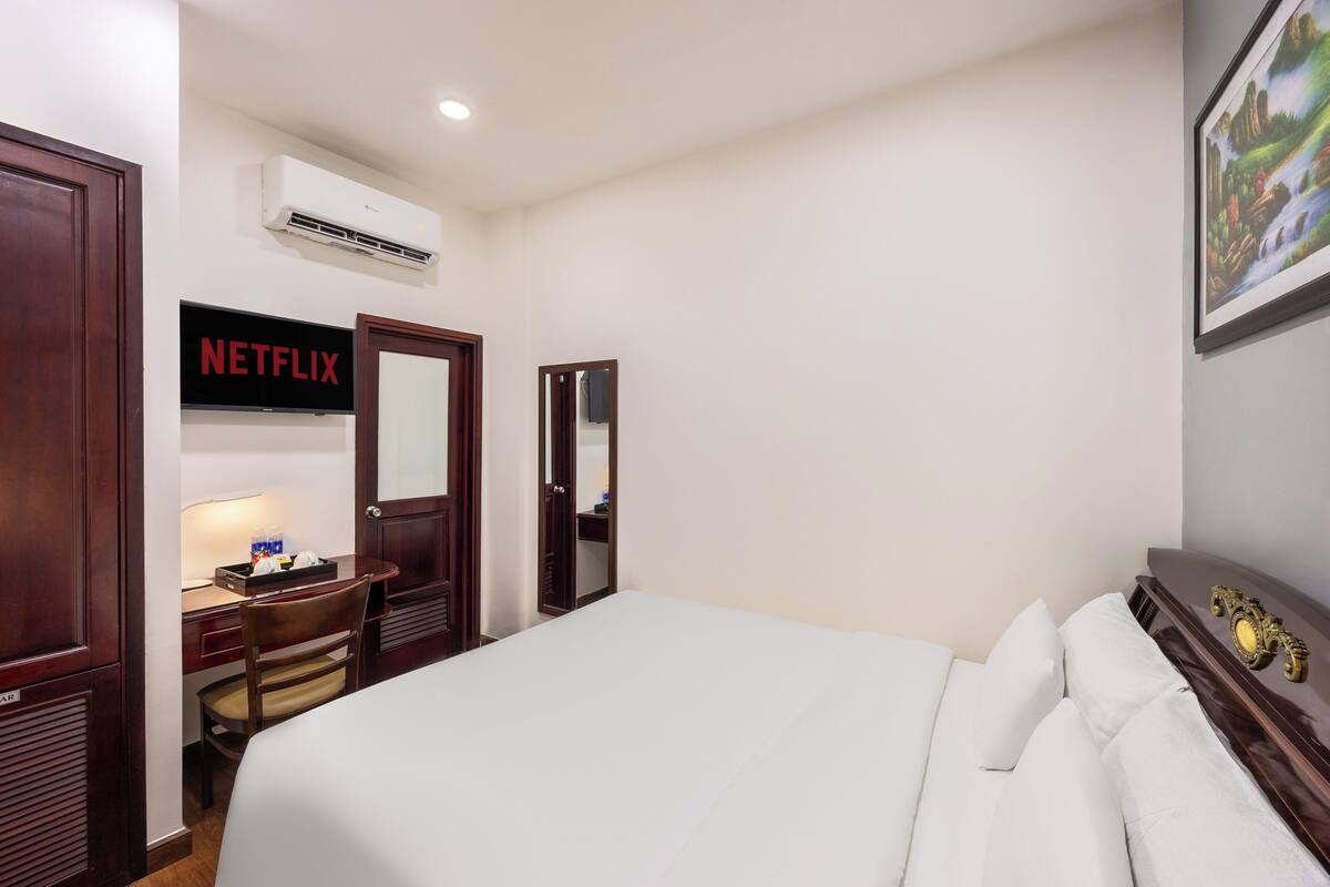 Une chambre d’hôtel avec un lit, un bureau avec une lampe, un miroir, un climatiseur et un tableau au mur.