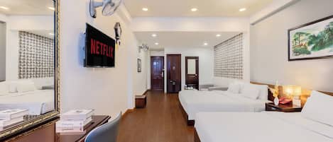 Habitación de hotel con un espejo grande, un televisor de pantalla plana, dos camas, un escritorio con una silla y un ventilador de techo.