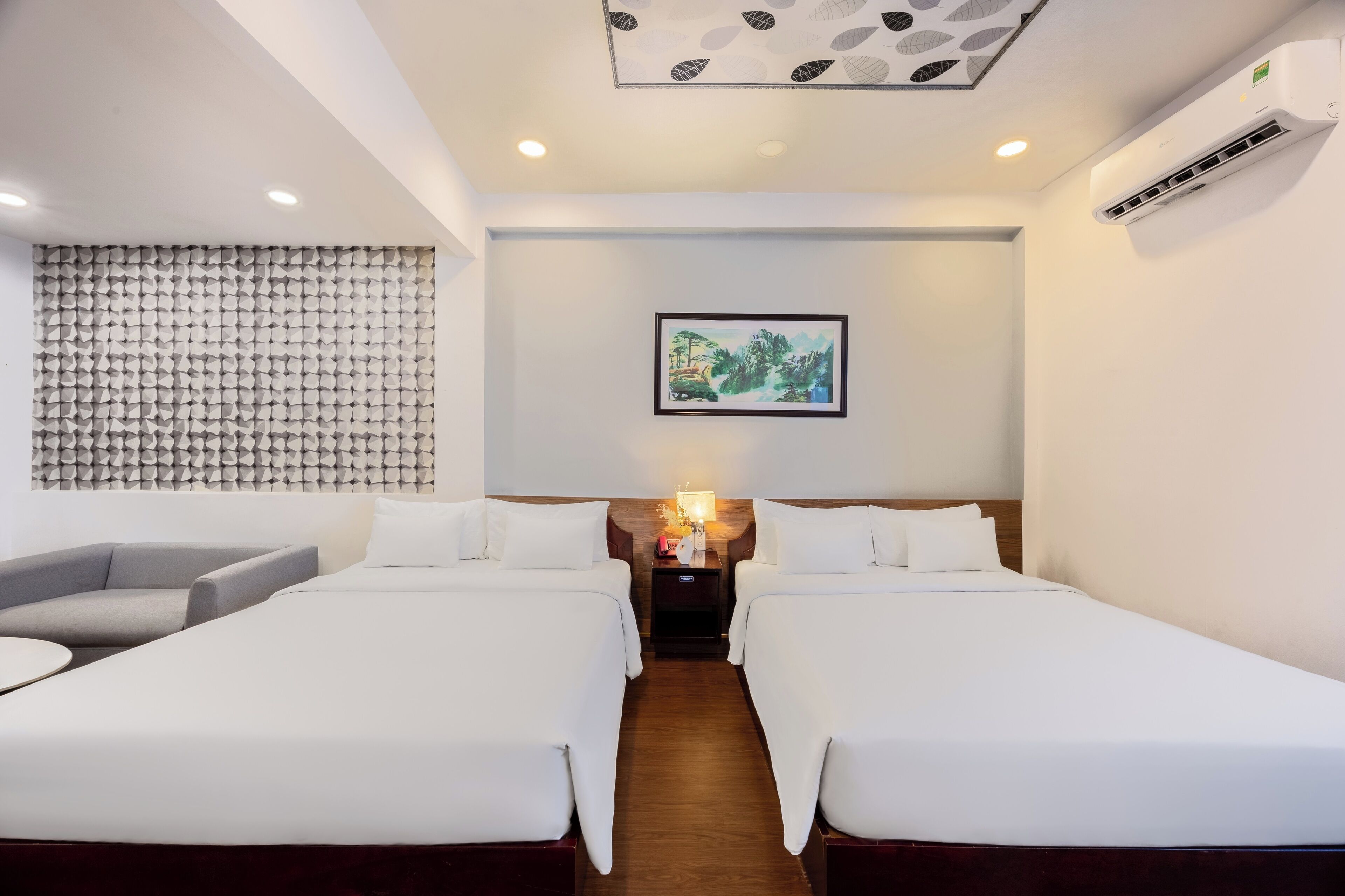 A hotel room with two beds, a sofa, a wall-mounted air conditioner, and a ceiling light fixture.