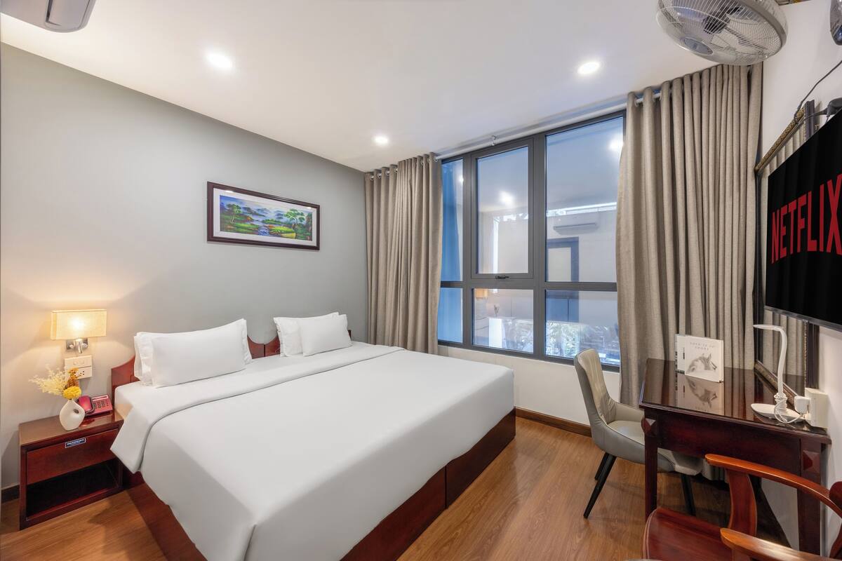 Une chambre d’hôtel comprenant un lit, une table de chevet, une lampe et un bureau avec une chaise.