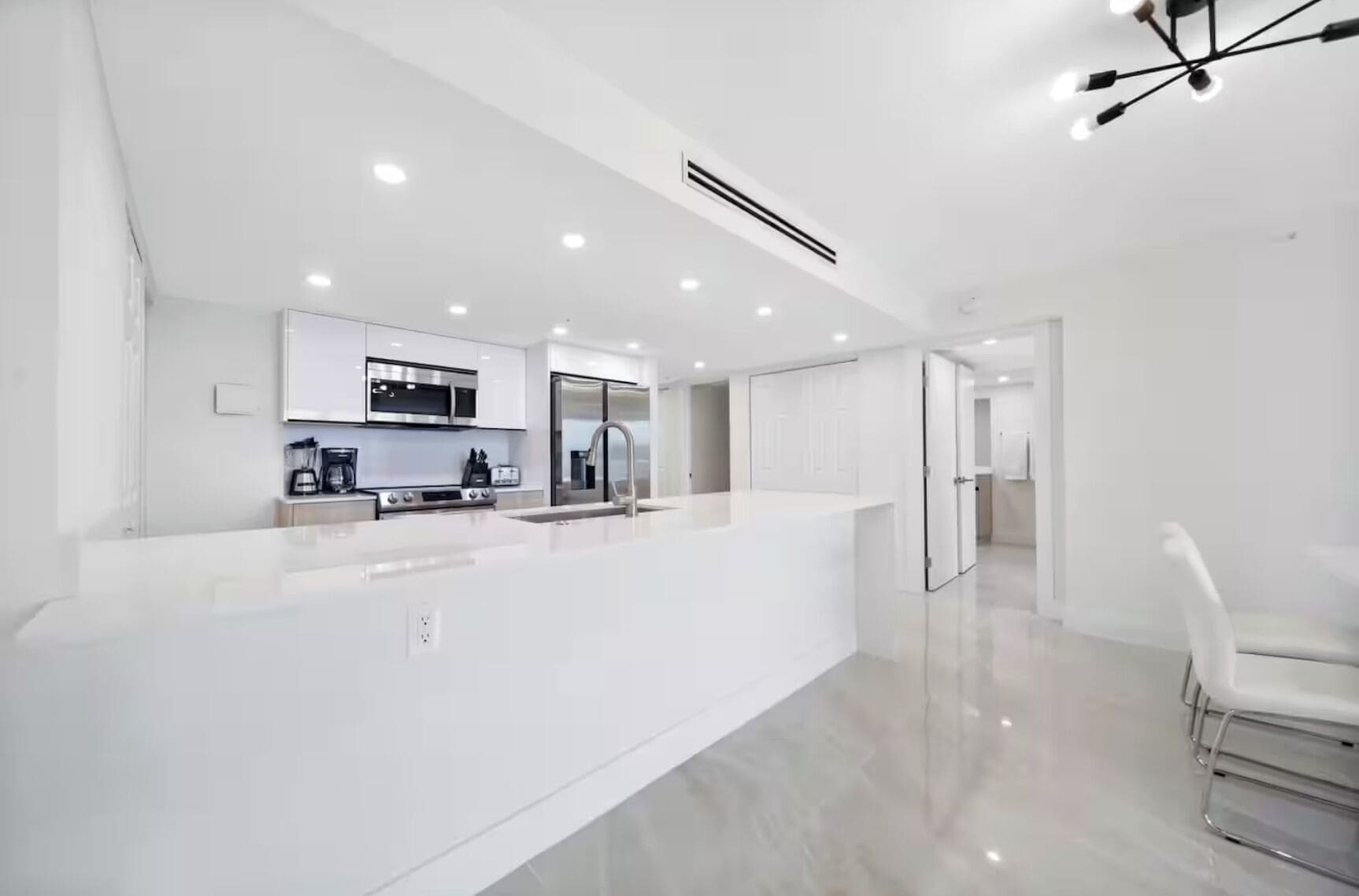 A modern kitchen with white cabinetry, stainless steel appliances, and a large island.