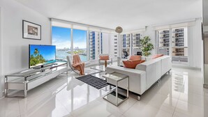 Een moderne woonkamer met een grote televisie, witte meubels en uitzicht op de stad.