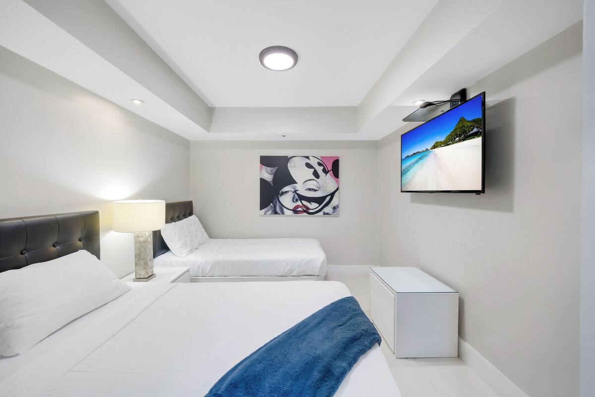 A modern hotel room with a large bed, a smaller bed, a TV, a painting, and a nightstand.