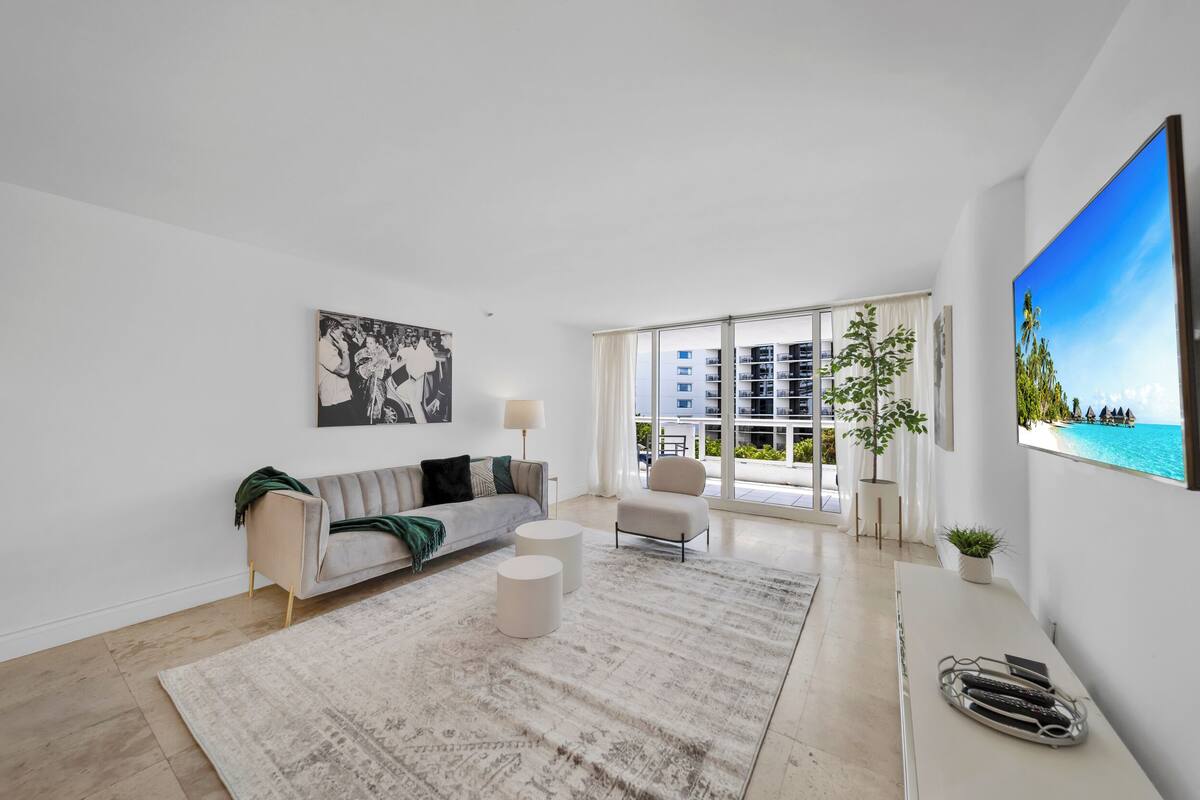 A modern living room with a sofa, two round coffee tables, a large window with a view of a building, and a painting on the wall.