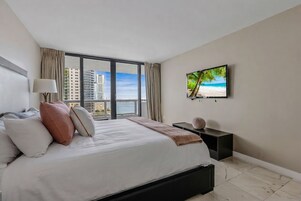 A hotel room with a large bed, a TV on the wall, and a view of the cityscape through the window.