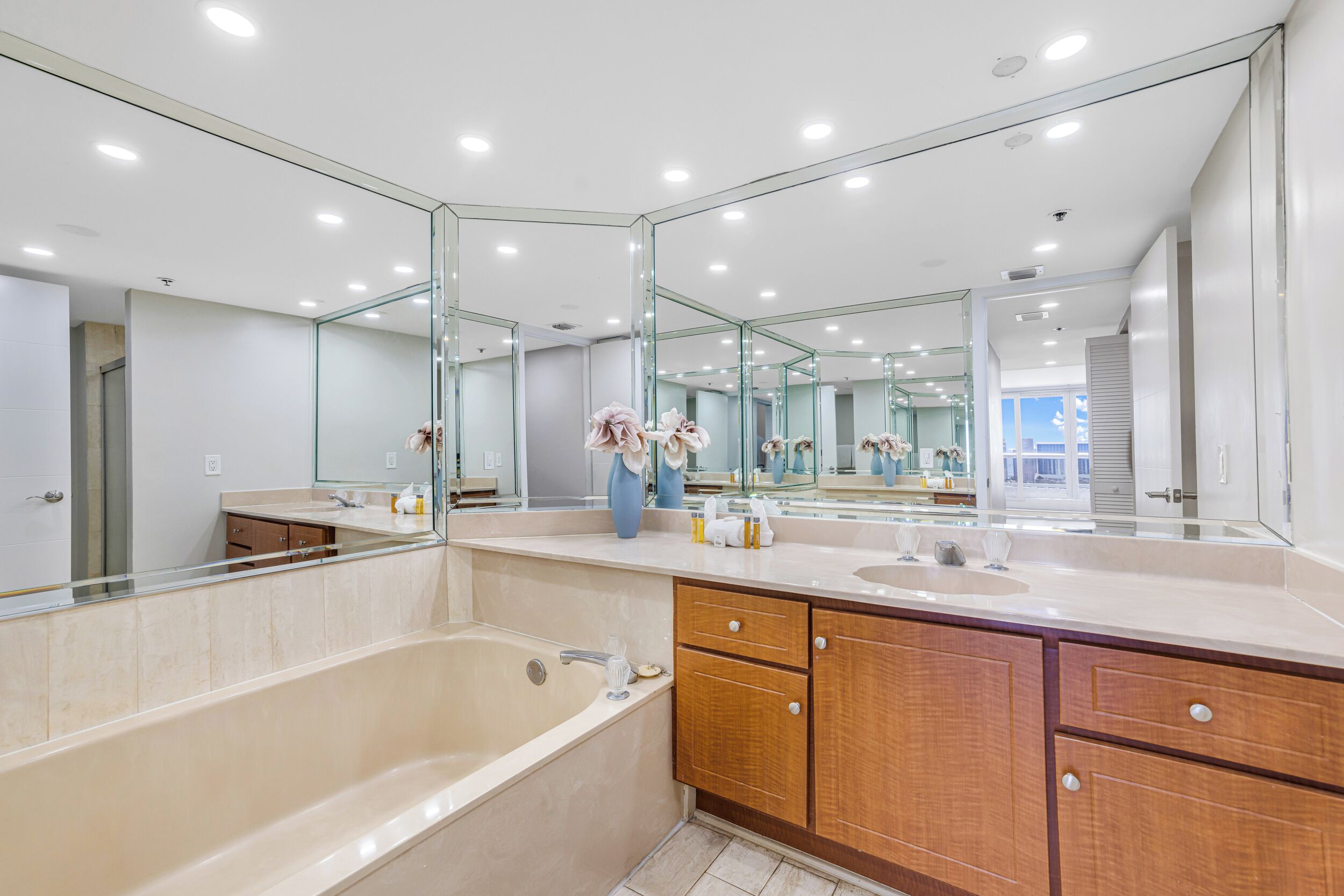 A modern bathroom with a large mirror, a bathtub, a sink, and wooden cabinets.