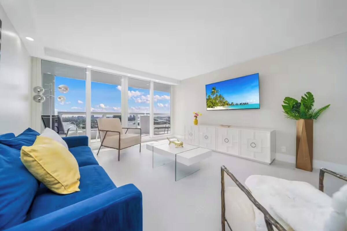 A modern living room with a blue sofa, a white coffee table, and a TV mounted on the wall.