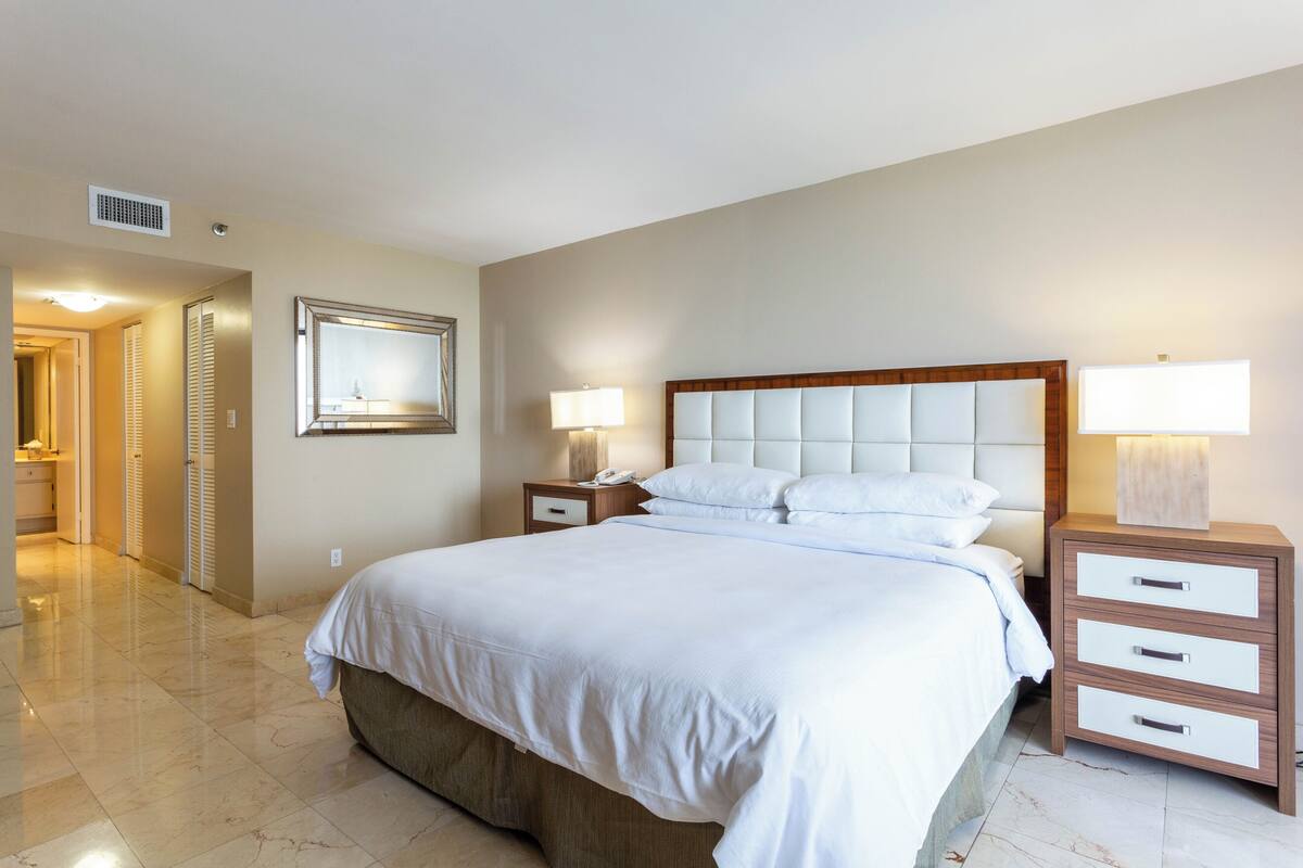 A hotel room with a large bed, bedside tables, a mirror, and a lamp.