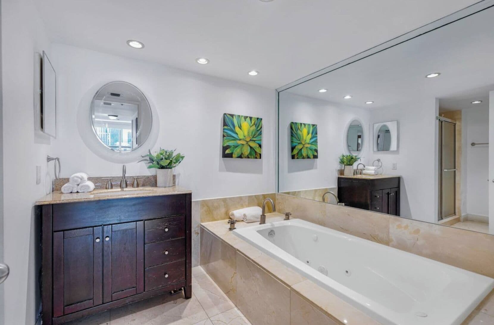 A modern bathroom with a large bathtub, dark wooden vanity, and two wall-mounted flower paintings.