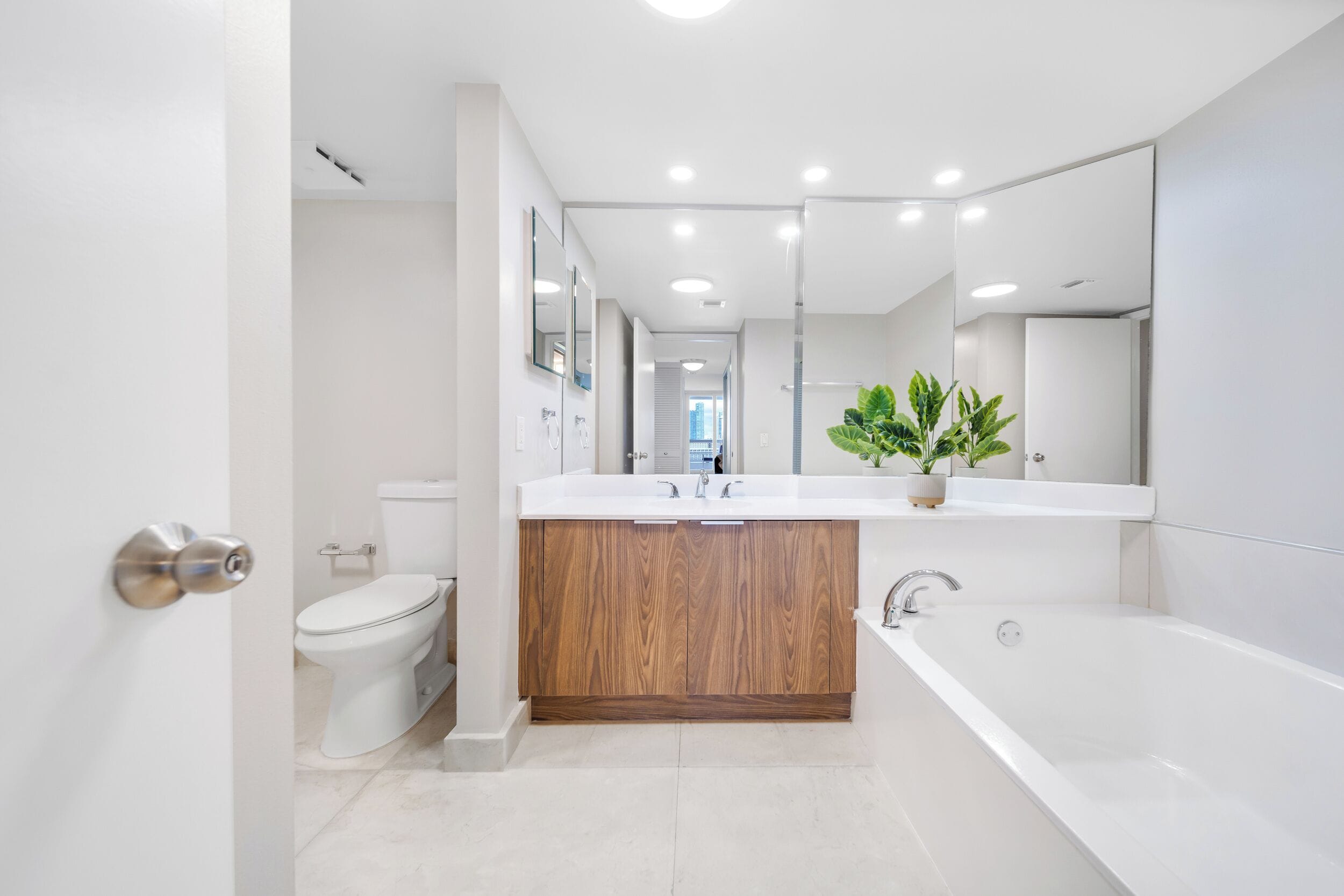 A modern bathroom with a white toilet, wooden vanity, and a large bathtub.