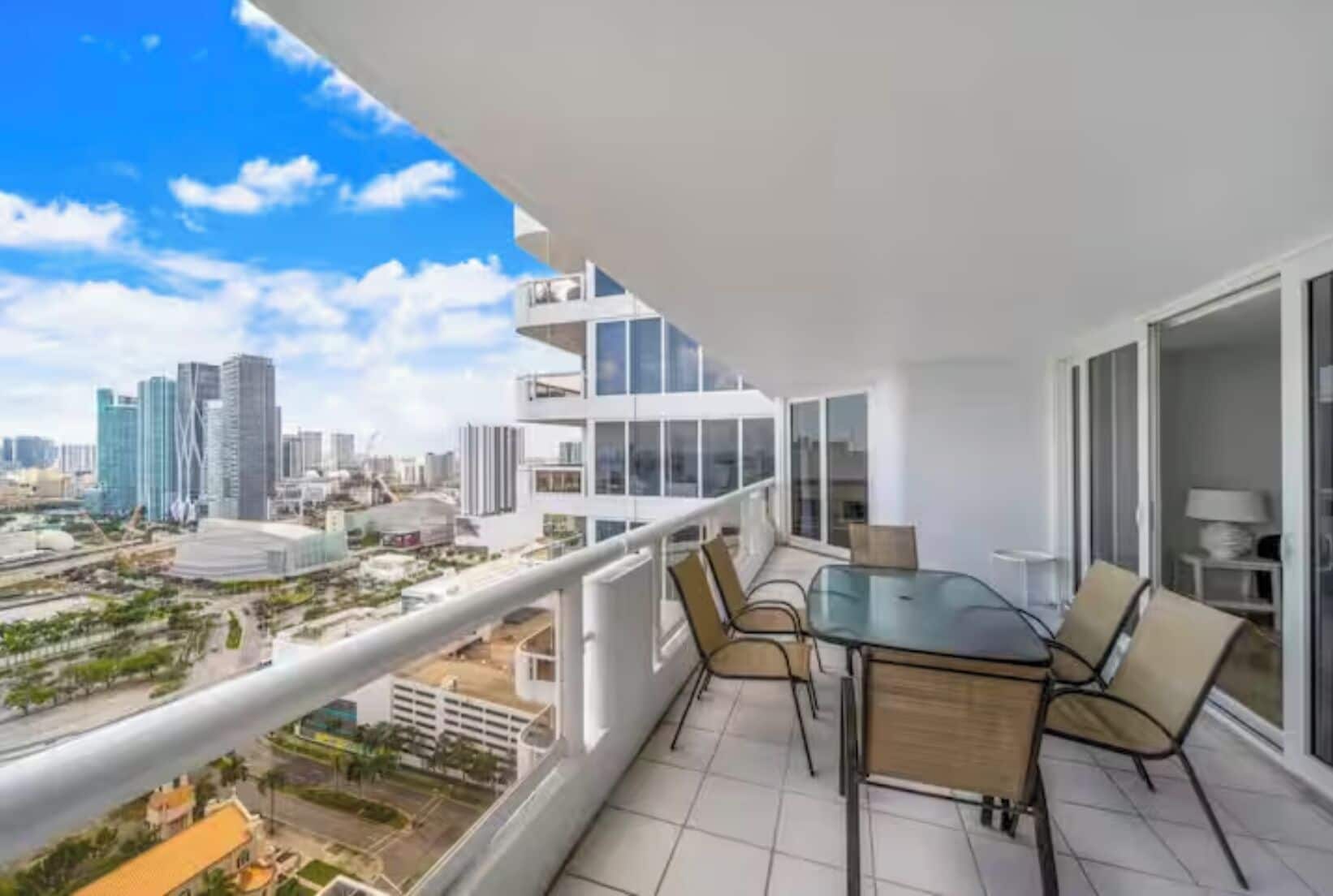 Un balcón con mesa y sillas, con vista a un paisaje urbano de edificios modernos.