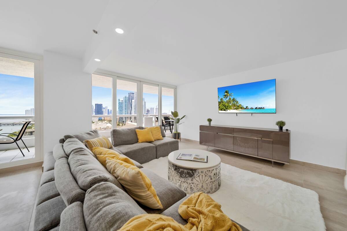 A modern living room with a large sofa, a round coffee table, and a flat-screen TV mounted on the wall.