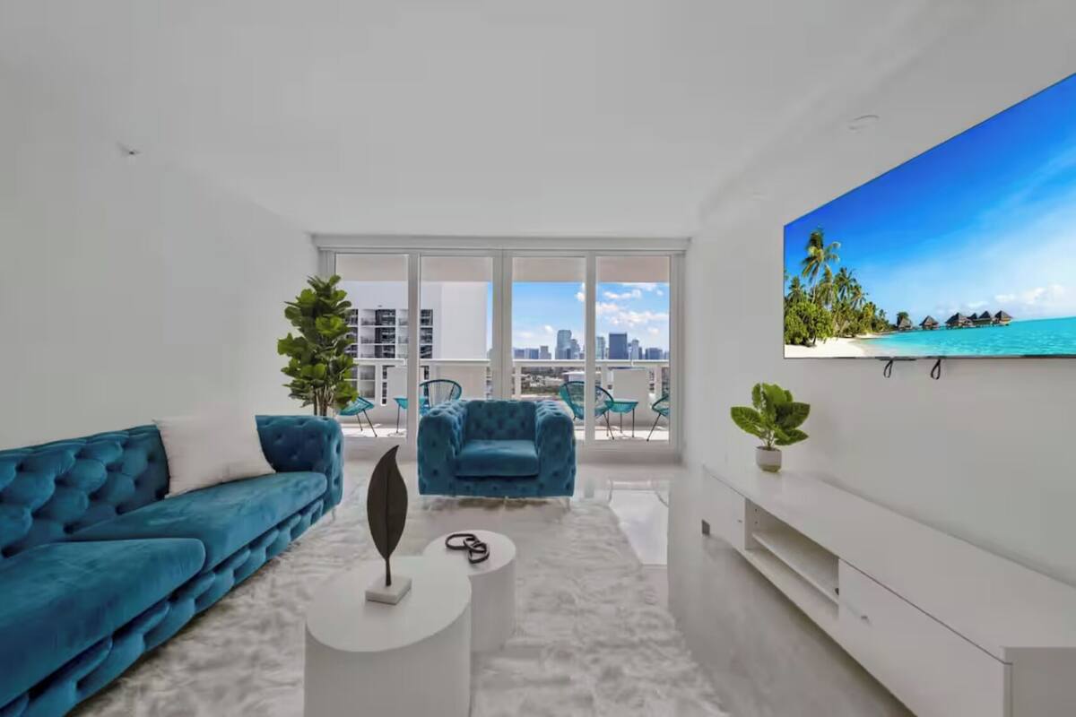 A modern living room with a blue sofa, a round coffee table, and a large TV screen displaying a tropical beach scene.