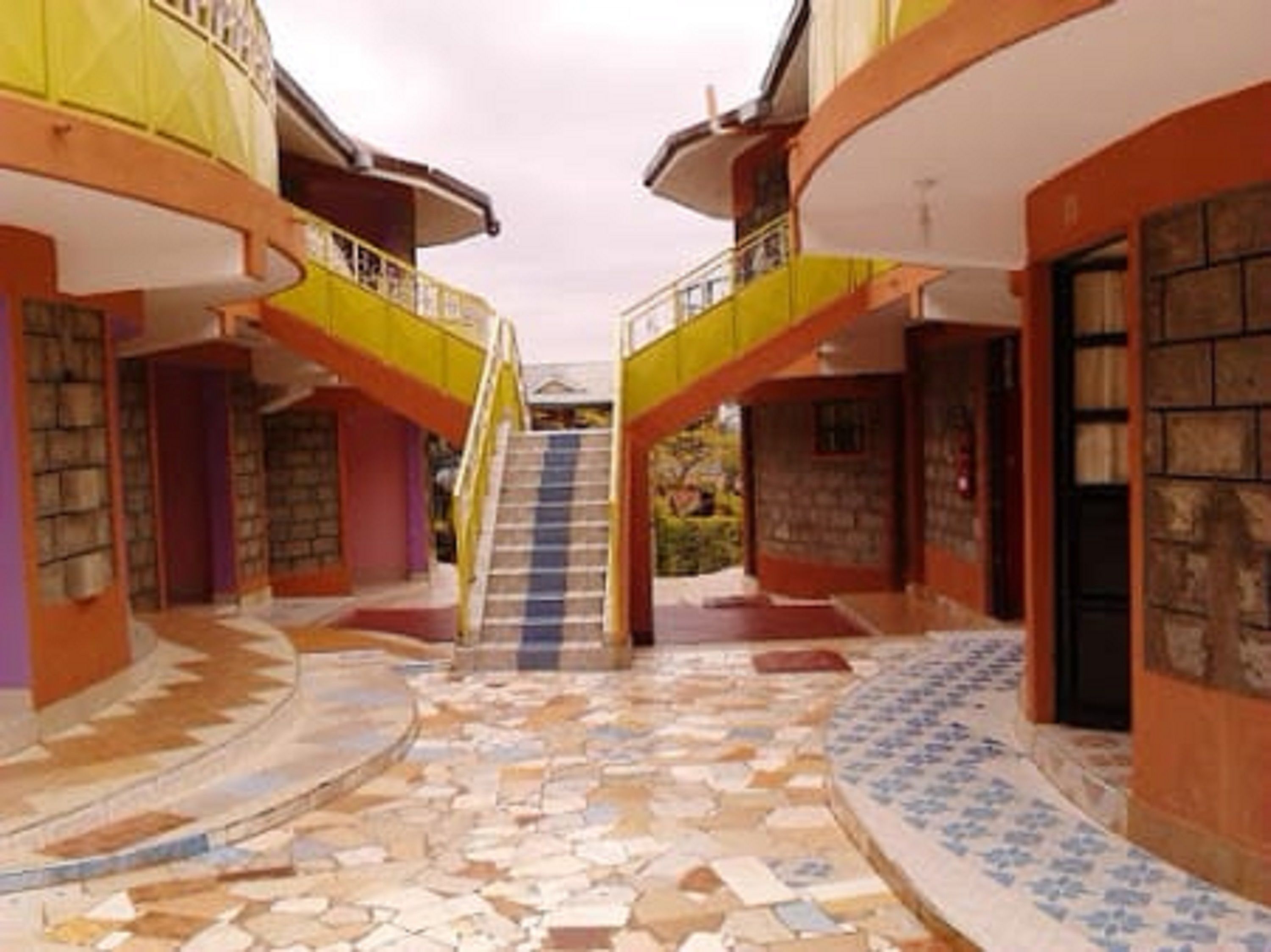 Un edificio con una escalera central que conduce a un nivel superior, rodeado de muros con fachada de piedra y suelo de baldosas.