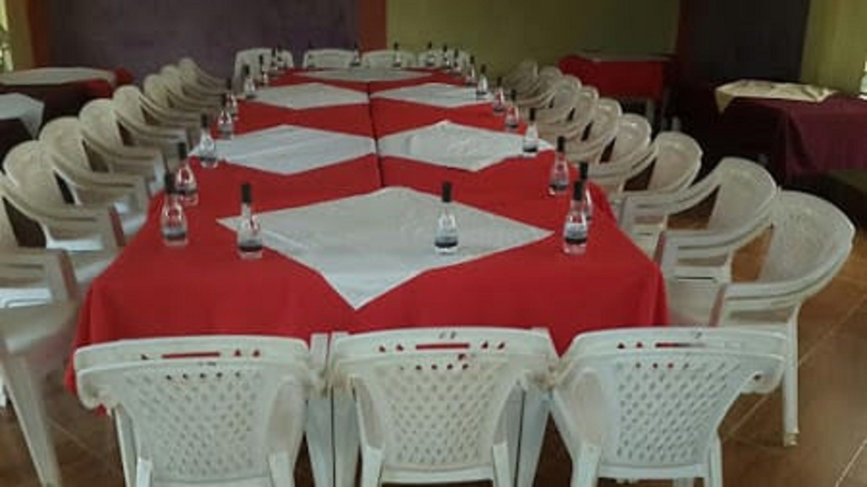 A conference room with a red tablecloth, white chairs, and water bottles on the table.