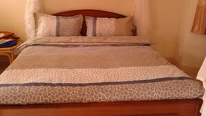 A bed with a canopy, a wooden headboard, and a patterned bedspread. - Jambo Village Hotel (Murang'a)