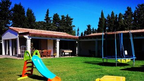 A playground with a slide and swings, a small table, and a building with a tiled roof.