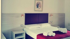 A bedroom with a bed, bedside tables, a nightstand, a red throw blanket, and a framed picture on the wall.