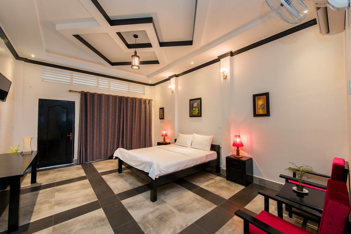 A bedroom with a bed, bedside tables, a desk, a chair, and a TV.