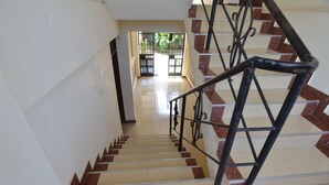 Una escalera con barandilla, suelo de baldosas estampadas en tonos beige y marrón, y vista a un espacio exterior con vegetación.
