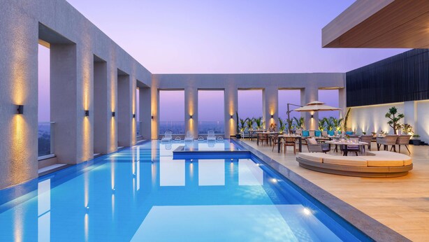 A modern indoor pool area with a long pool, lounge seating, and large windows.