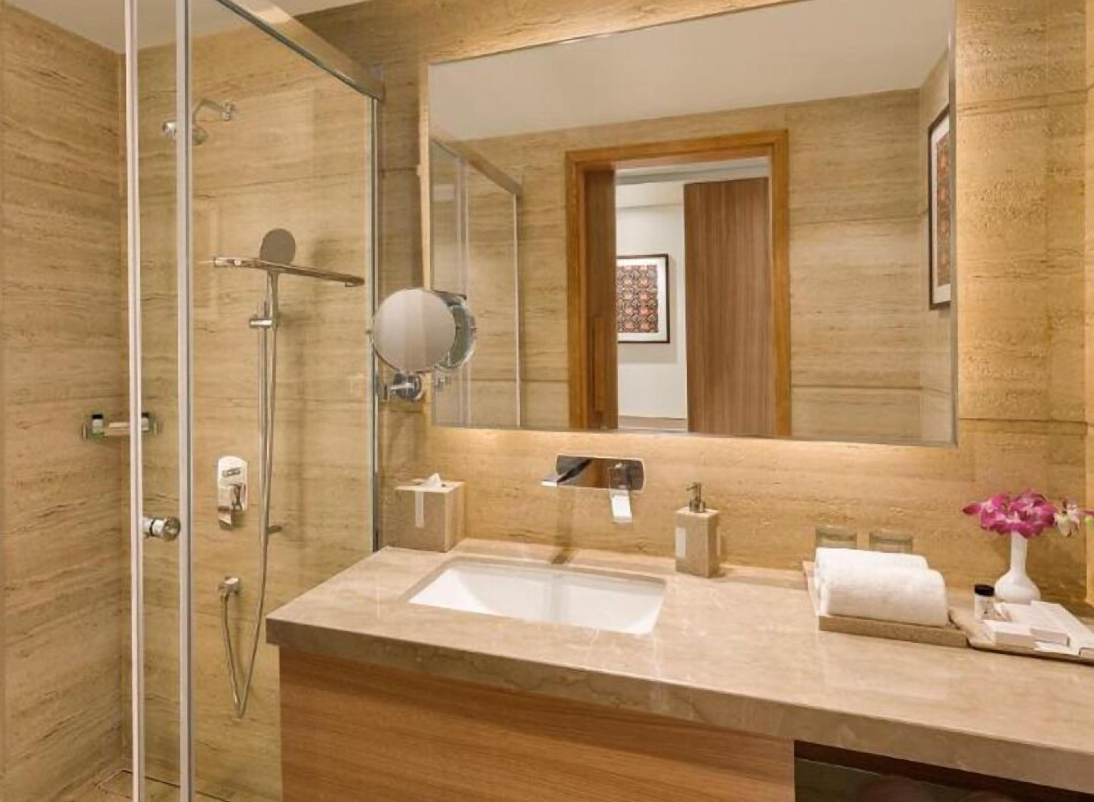A modern bathroom with a glass shower enclosure, a large mirror, and a marble countertop.