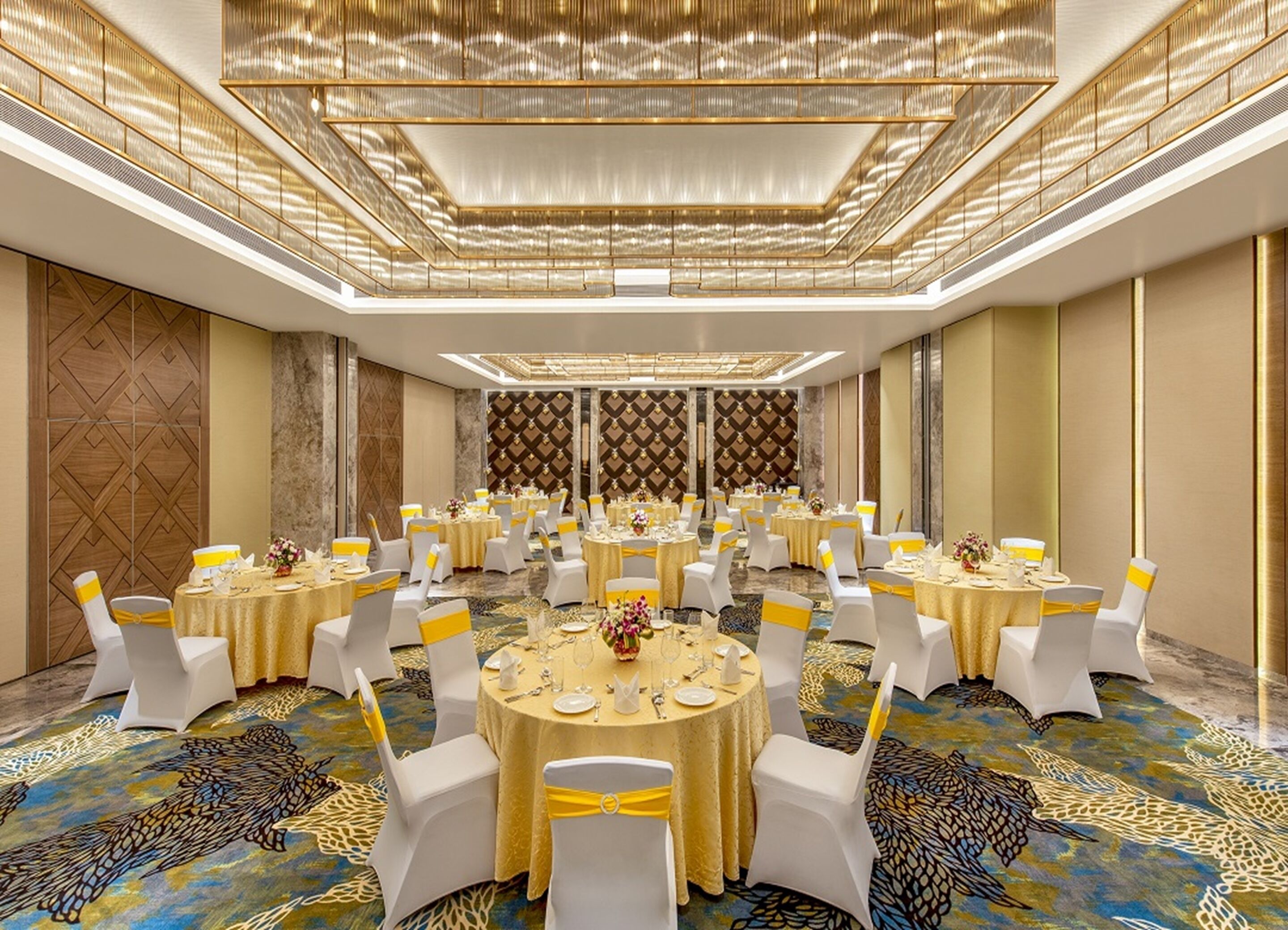 A banquet hall with round tables, white chairs, and yellow sashes.
