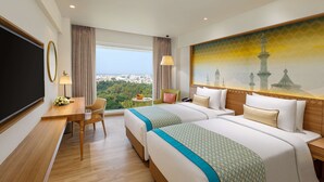A hotel room with two beds, a desk, a chair, a TV, and a large window with a city view.