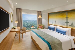 A hotel room with a large bed, a desk, a chair, and a view of a mountainous landscape.