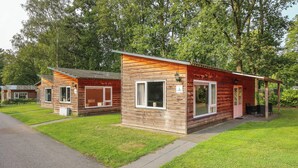 A row of wooden cabins with large windows, a covered porch, and a paved pathway. - Landgoed Leudal (Haelen)