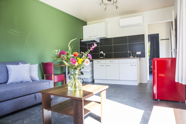 A modern living room with a sofa, a wooden coffee table with a vase of flowers, and a kitchen in the background. - Landgoed Leudal (Haelen)