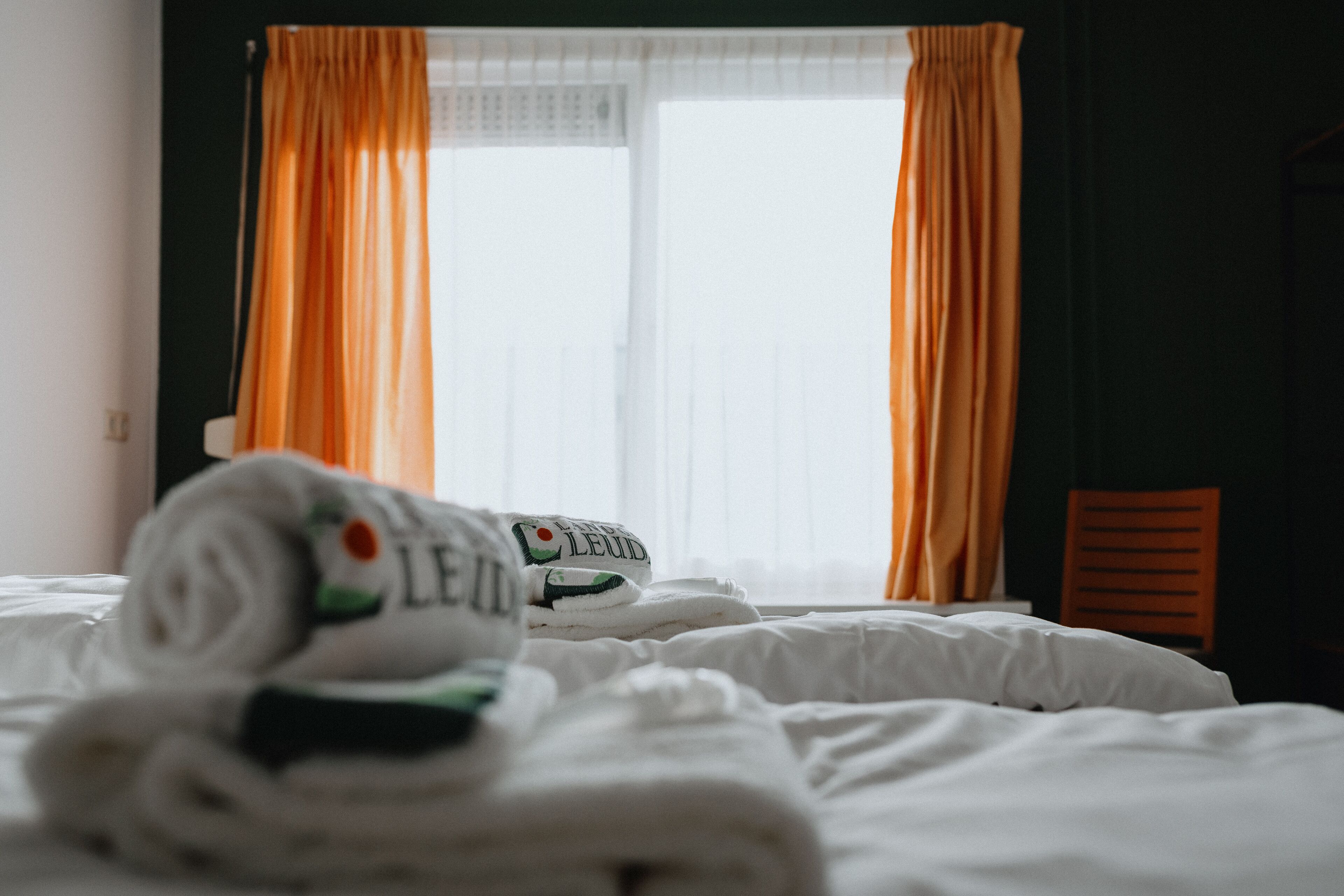 Une chambre d’hôtel avec un lit, une fenêtre avec des rideaux et une serviette sur laquelle est imprimé un texte.