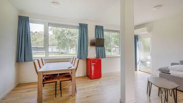 Een kamer met een houten eettafel, stoelen, een rode koelkast, een televisie aan de muur en een bank.