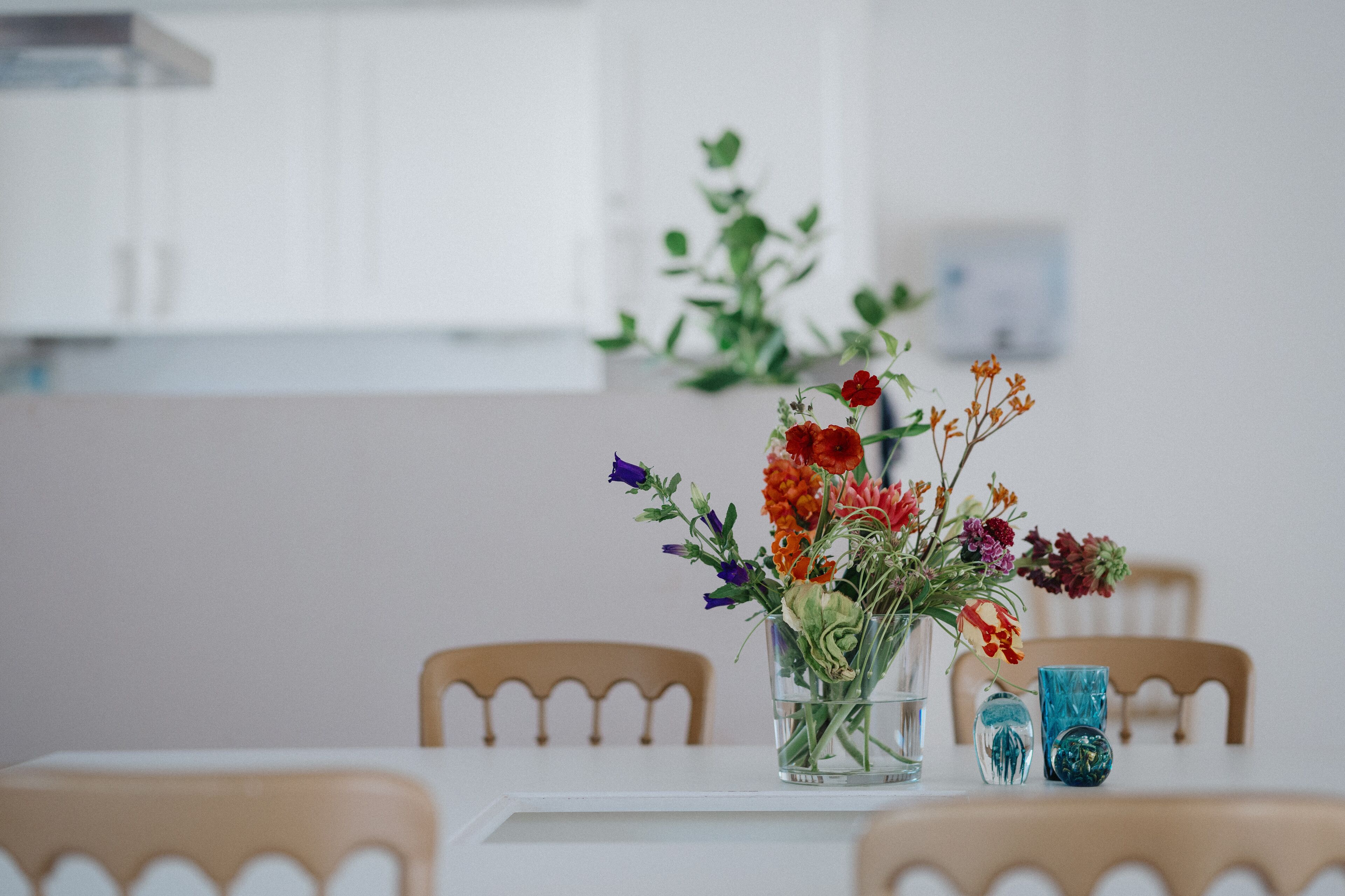 A dining table with a clear glass vase containing a variety of flowers.