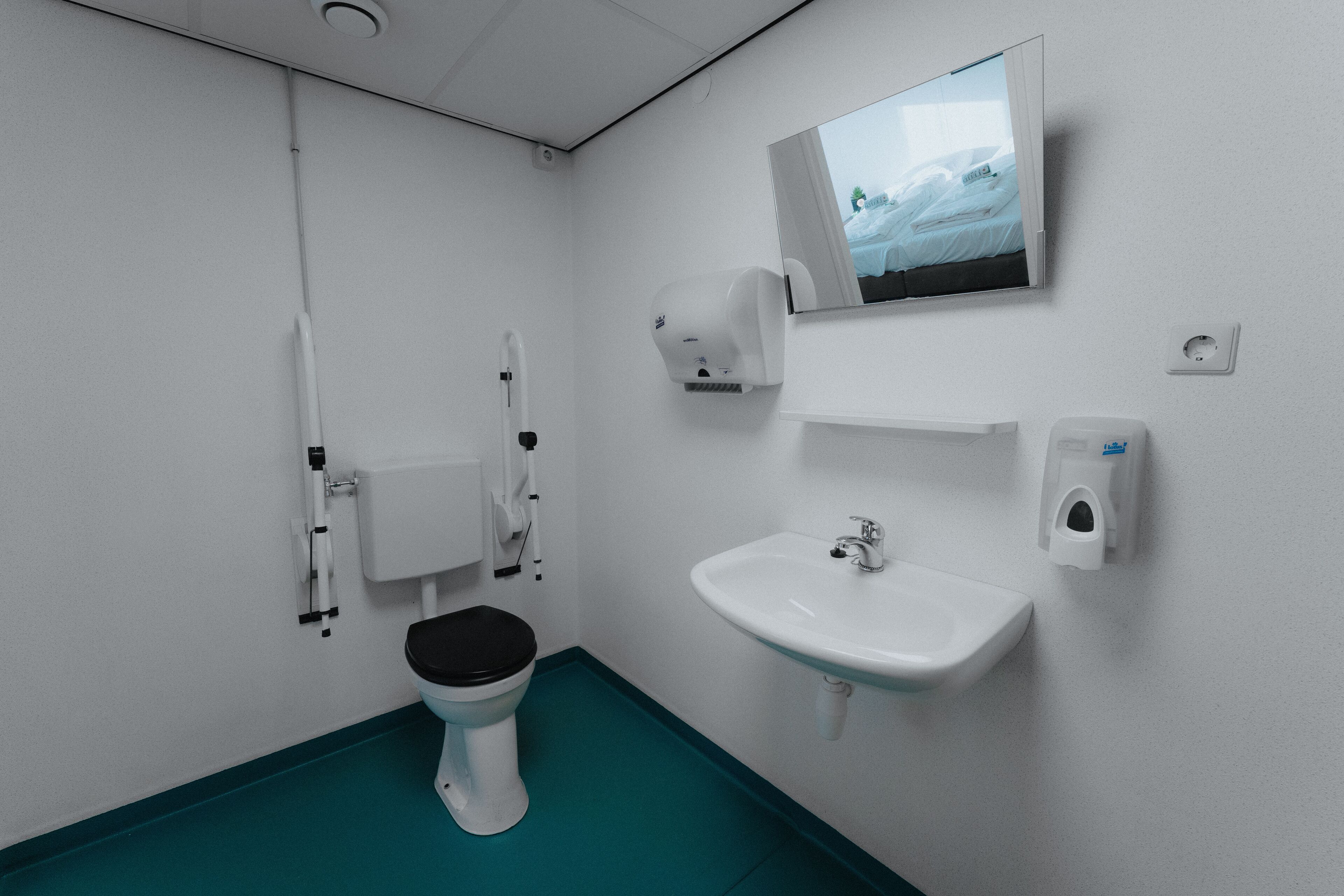 Een moderne badkamer met toilet, wastafel, handdroger en spiegel met uitzicht op een raam.