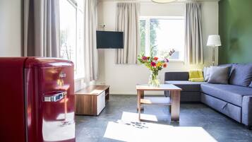 A modern living room with a sofa, a coffee table, a red refrigerator, and a flat-screen TV mounted on the wall.