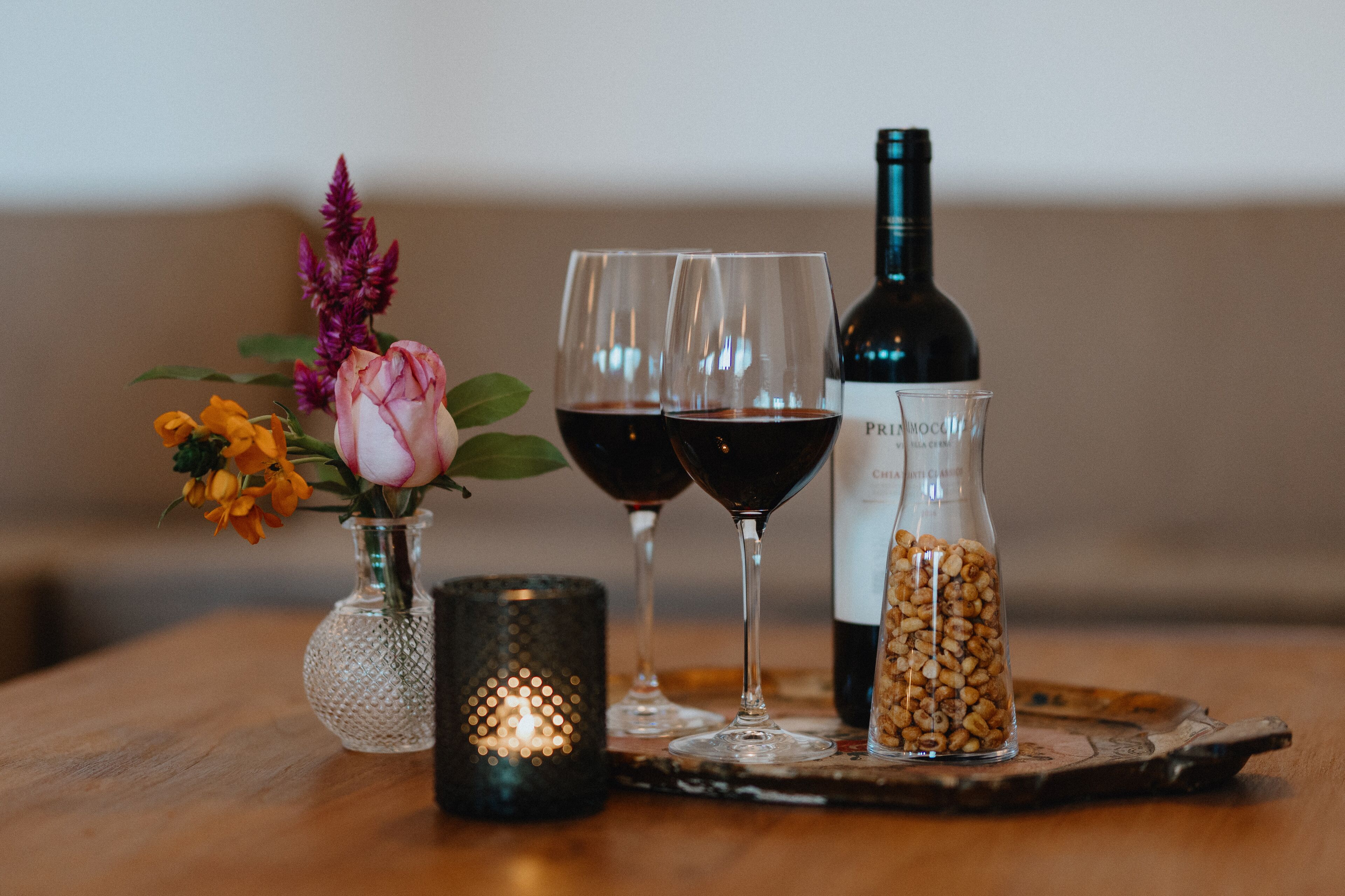 Uma mesa com uma garrafa de vinho, dois copos de vinho, uma vela e um vaso com flores.