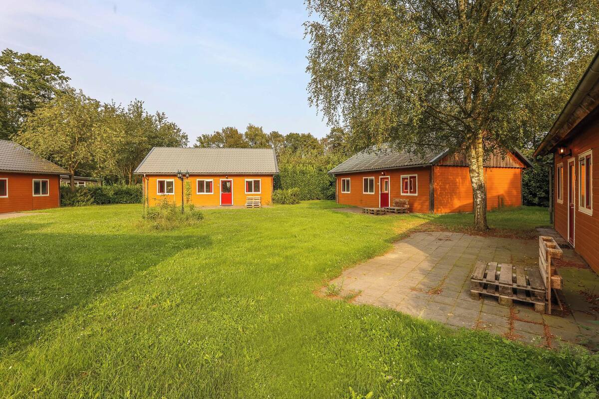 Un barrio residencial con tres casas de madera, cada una con una puerta roja y un pequeño jardín delantero.