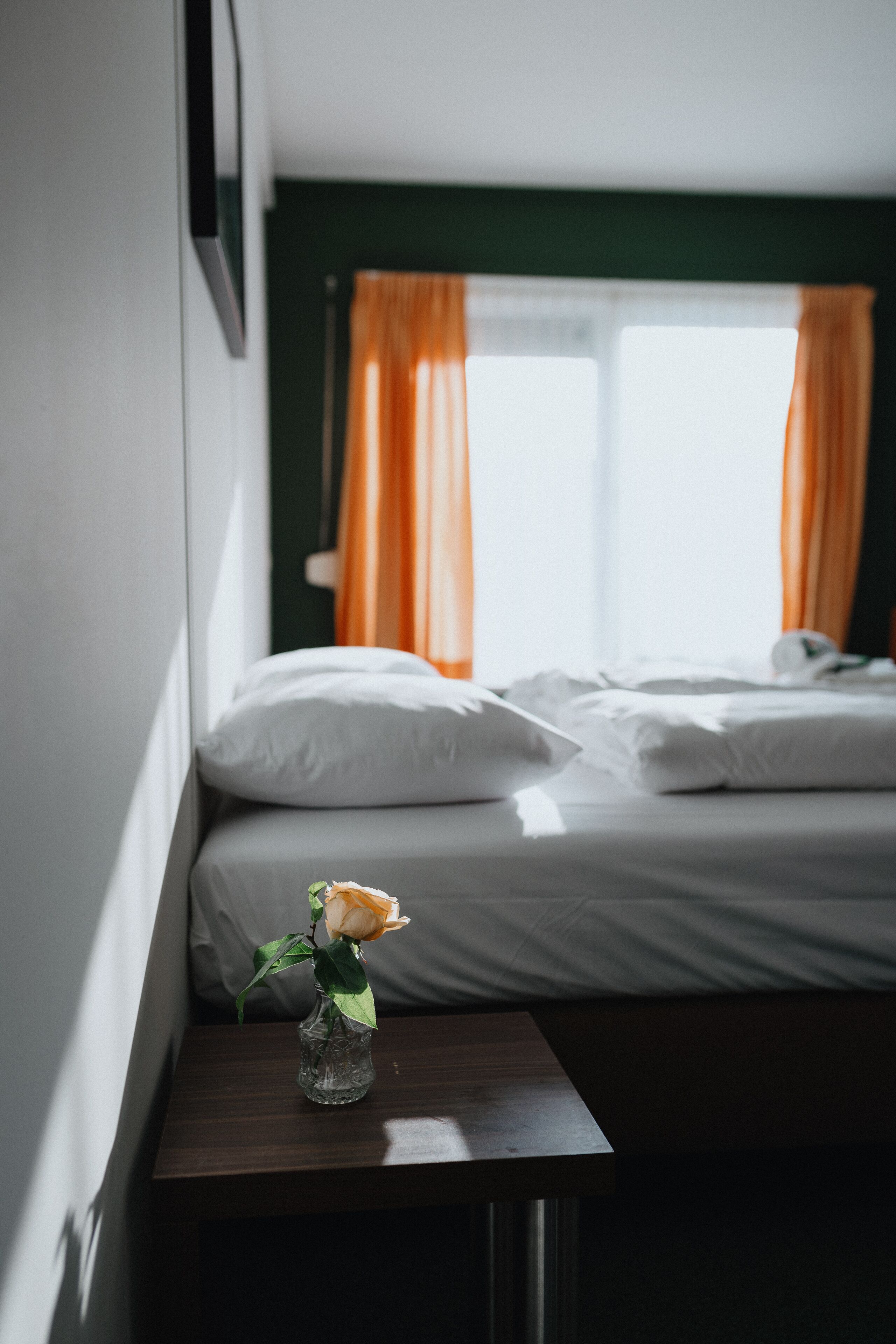 Habitación de hotel con cama, mesita de noche con un florero y ventana con cortinas.