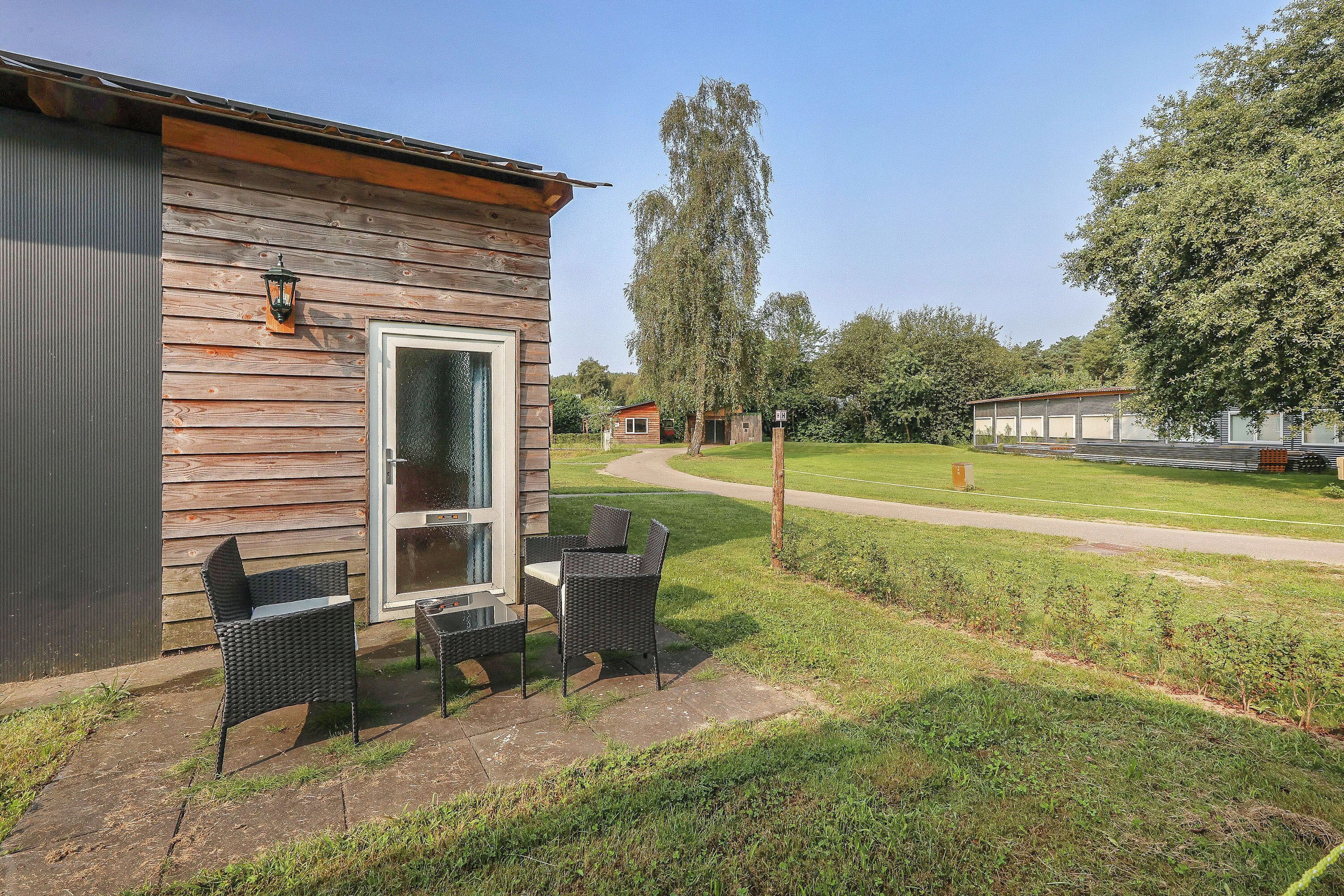 A wooden cabin with a patio area featuring two wicker chairs and a table.