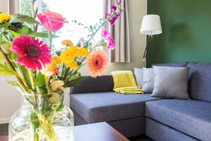 A living room with a grey sofa, a yellow throw blanket, and a vase of flowers. - Landgoed Leudal (Haelen)