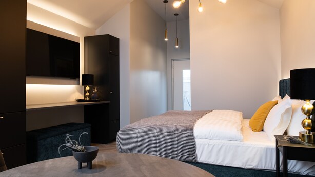 Quarto moderno com cama, mesa de cabeceira e escrivaninha. Há uma cadeira e uma pequena mesa com um vaso.