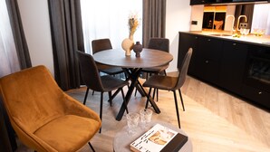 Uma área de refeições moderna com uma mesa redonda, quatro cadeiras, um vaso com flores secas e uma revista sobre uma mesinha lateral.