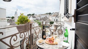 A balcony with a table set for a meal, including a bottle of wine, glasses, and a plate of food. - Perlage Suite Luxury B&B (Alberobello)