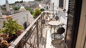 A balcony with a table and chairs, potted plants, and a view of a town with white buildings and a statue. - Perlage Suite Luxury B&B (Alberobello)